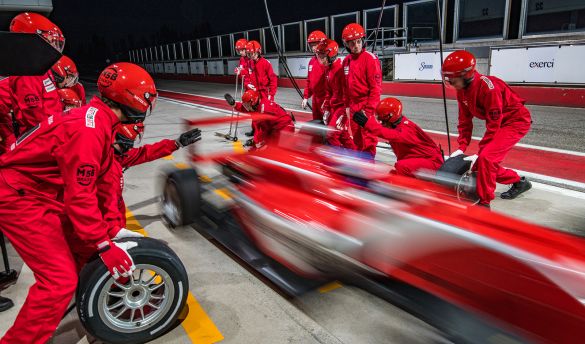 Racing team in red uniforms change tires of a red racing car during pit stops