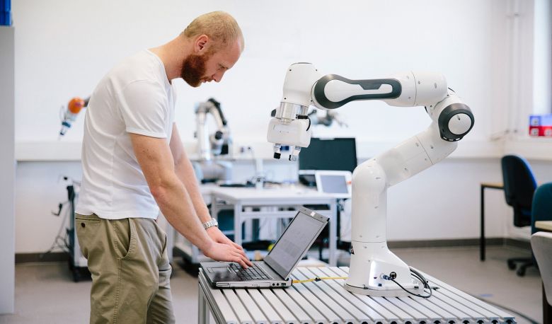 Man standing in front of a laptop and a robotic arm