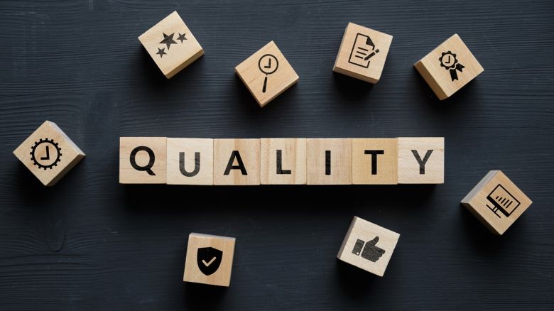 Wooden cubes with letters and symbols on a black table and form the word Quality