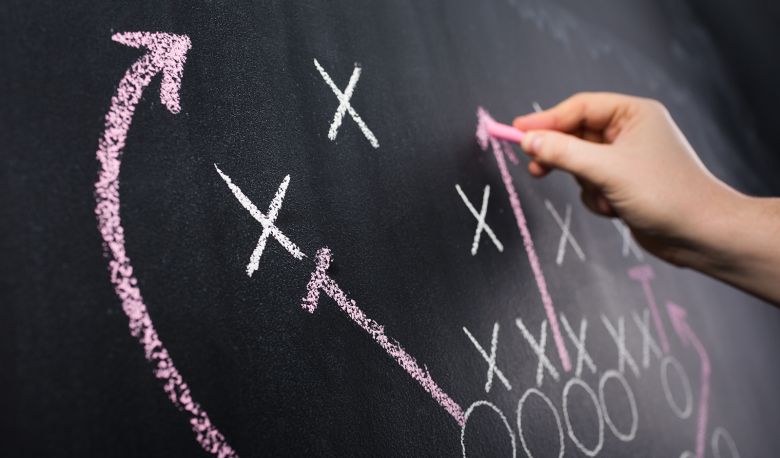 Hand draws a game strategy with chalk on a blackboard